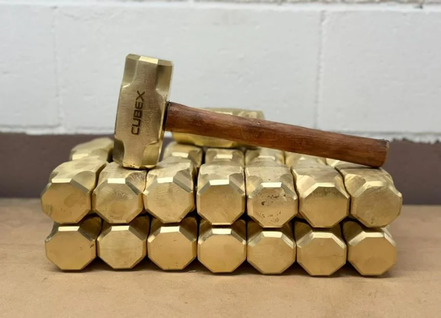 Marreta de bronze CUBEX apoiada sobre dezenas de cabeças de marreta empilhadas.